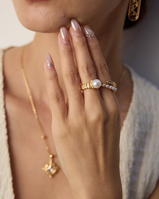 Close-up of a woman's hand wearing gold jewelry with a neutral background