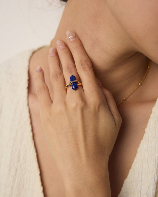 Close-up of a hand wearing a blue gemstone ring with a blurred background
