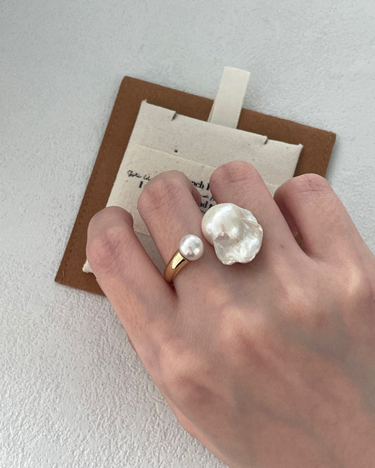 Hand wearing a pearl ring with a plain background