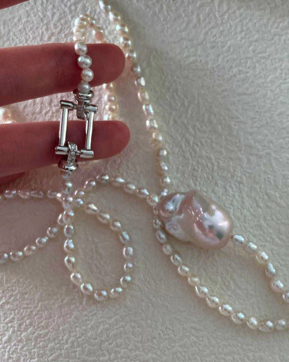 Pearl necklace with a pink pearl pendant held by a hand on a light background