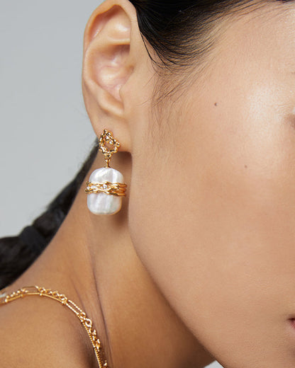 Close-up of a woman wearing gold earrings and necklace against a neutral background