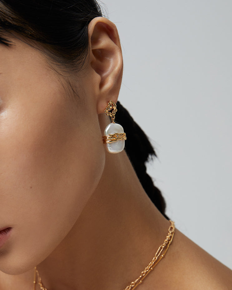 Woman wearing gold jewelry with a neutral background
