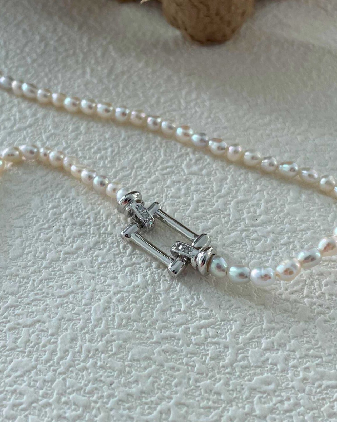 Pearl necklace with a silver clasp on a textured beige surface