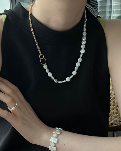 Person wearing a black sleeveless top with a pearl necklace and bracelet, sitting on a couch.