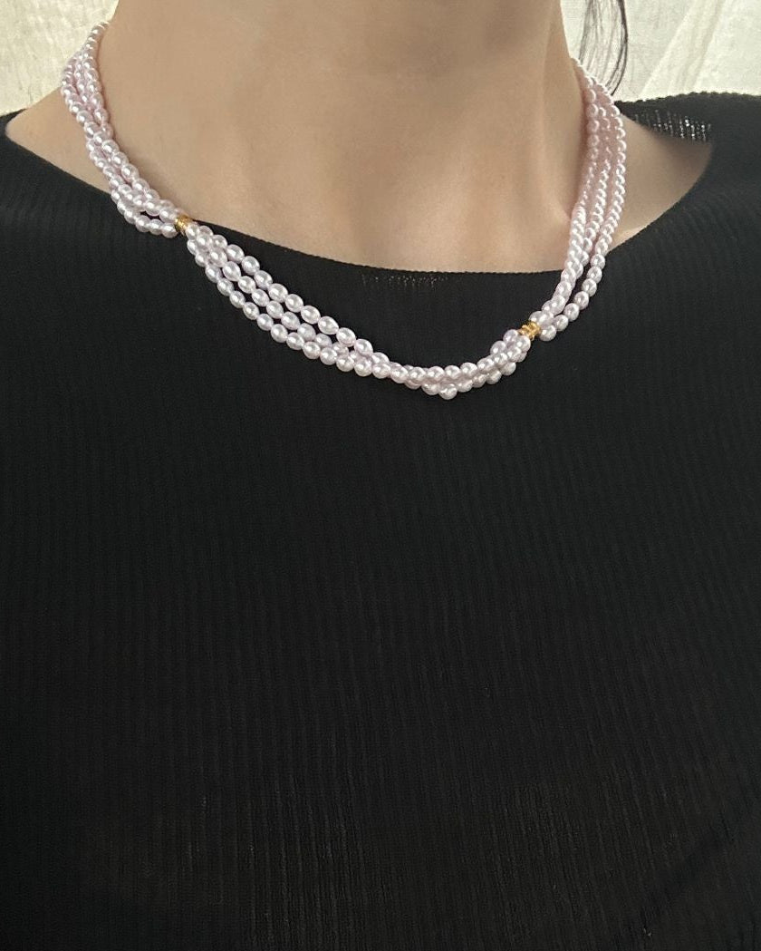 Person wearing a black top with pearl necklaces and bracelet indoors.