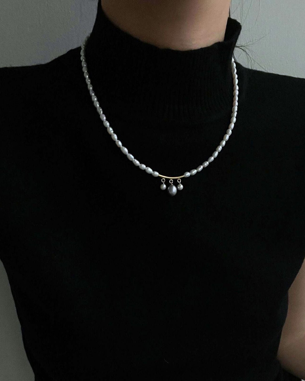 Person wearing a black turtleneck with a pearl necklace against a neutral background