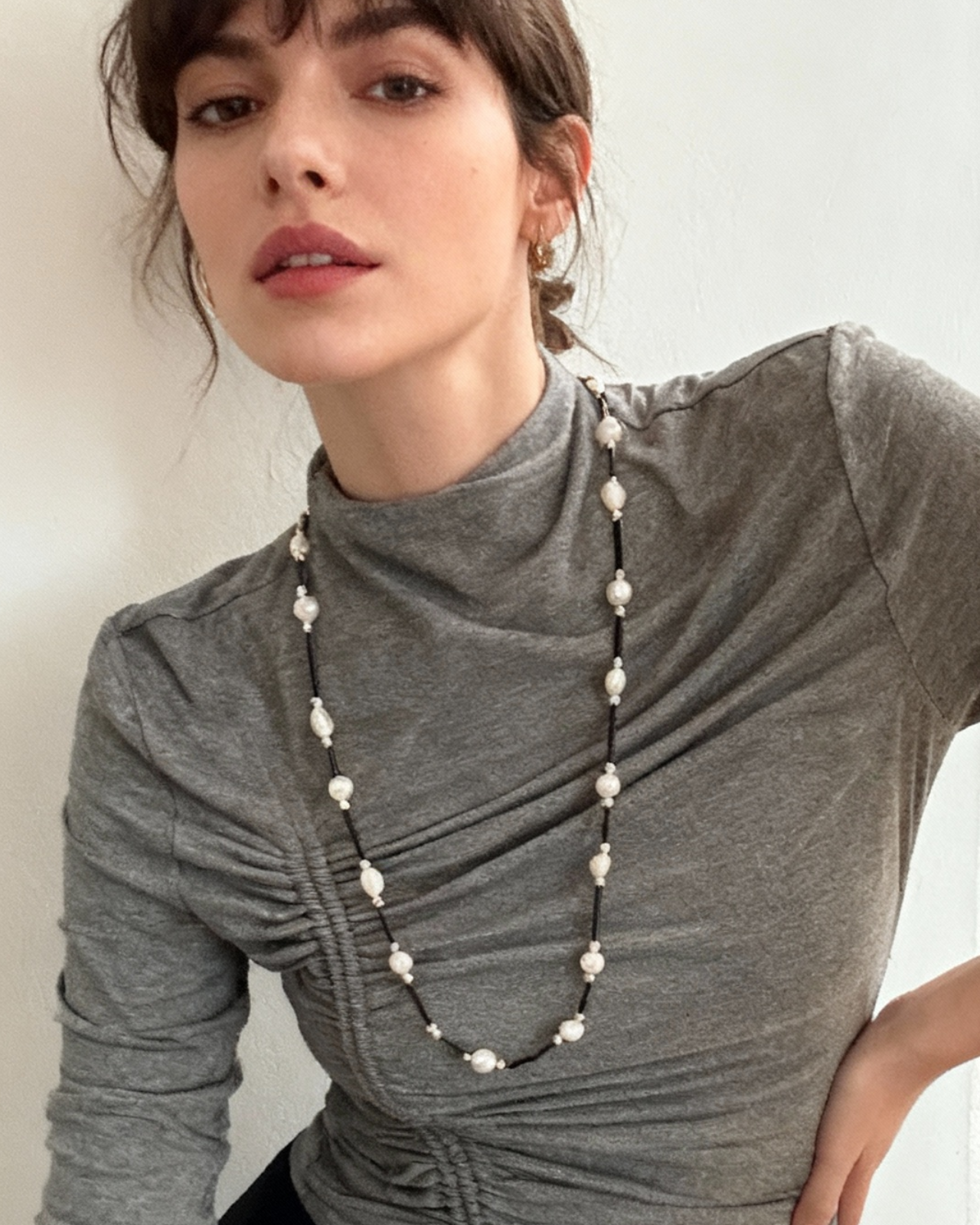 Woman wearing a long pearl necklace against a plain background