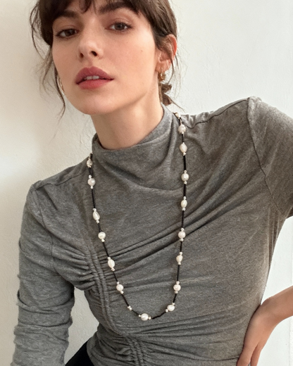 Woman wearing a long pearl necklace against a plain background
