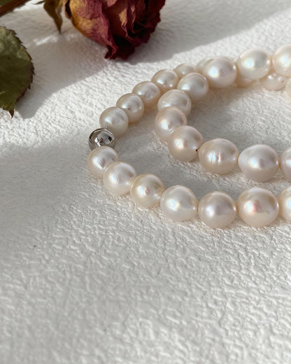 Pearl necklace on a textured white surface with a dried rose and leaves.