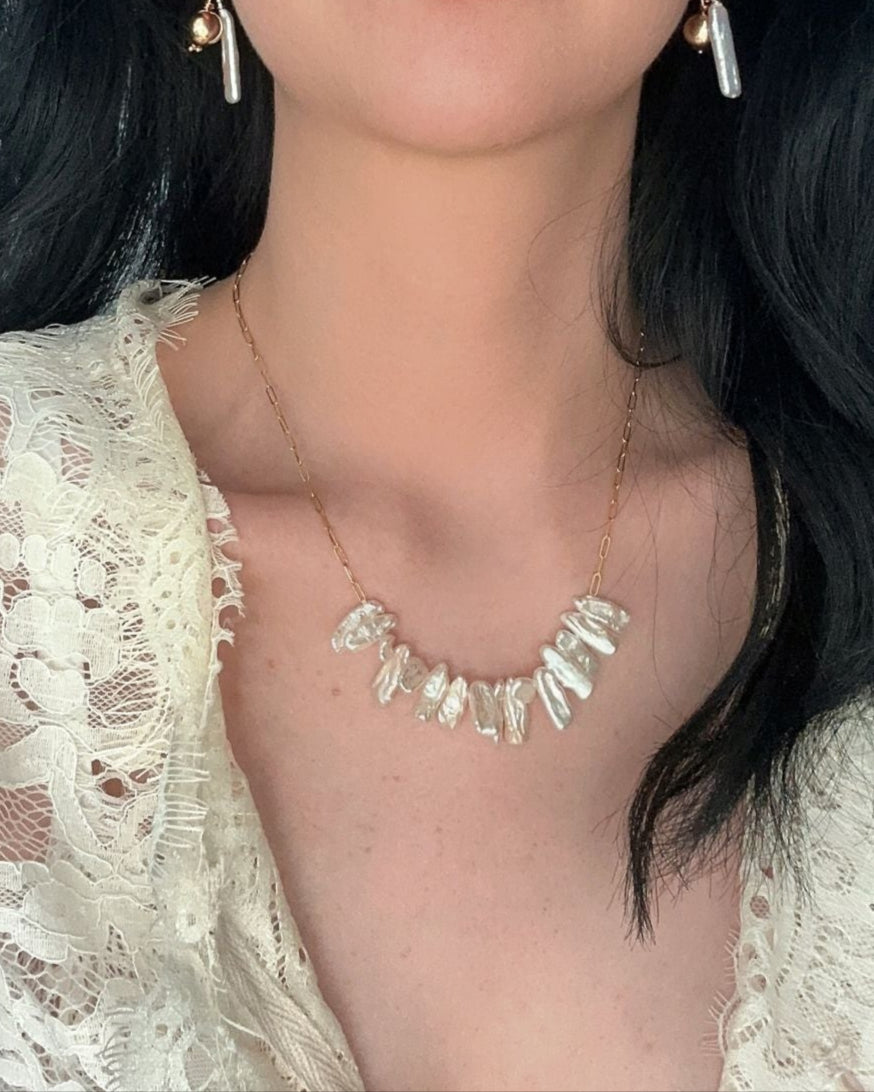 Woman wearing a lace top and necklace with earrings indoors.