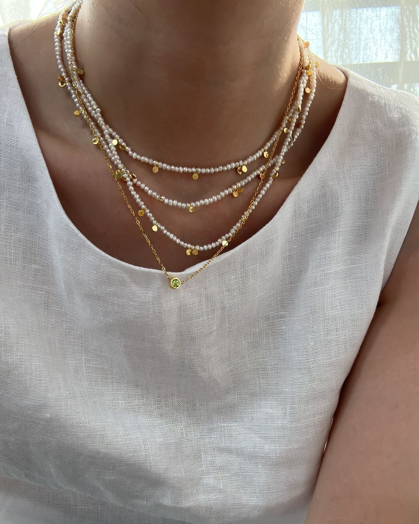 Necklace with small yellow beads worn by a person in a white top.