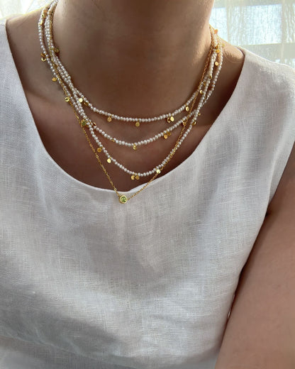 Necklace with small yellow beads worn by a person in a white top.