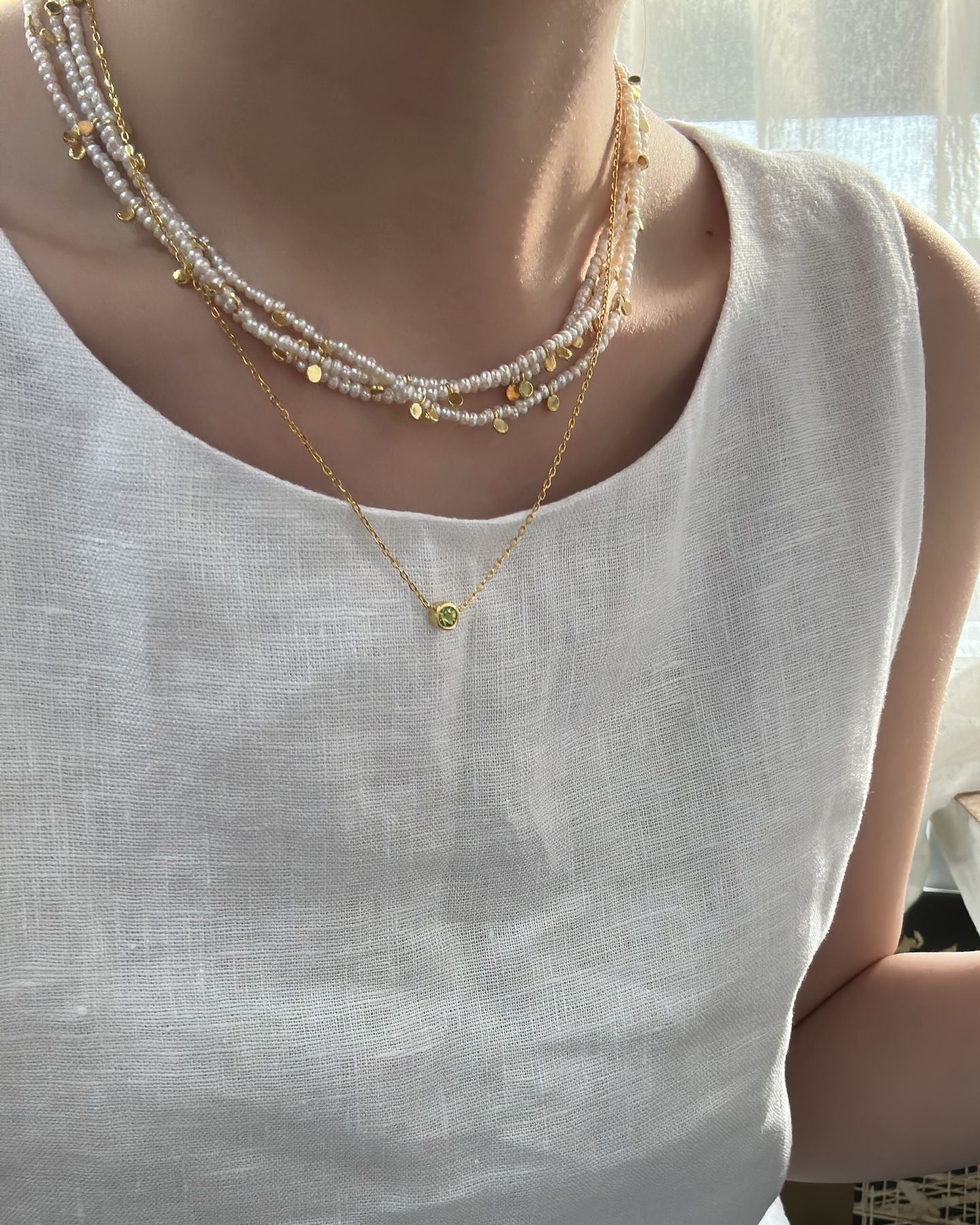 Person wearing a white sleeveless top with layered necklaces.