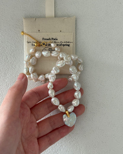Pearl necklace held by a hand with a branded card in the background