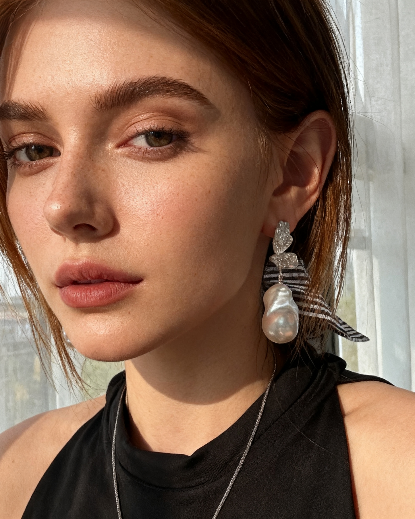 Close-up of a person wearing earrings with a blurred outdoor background