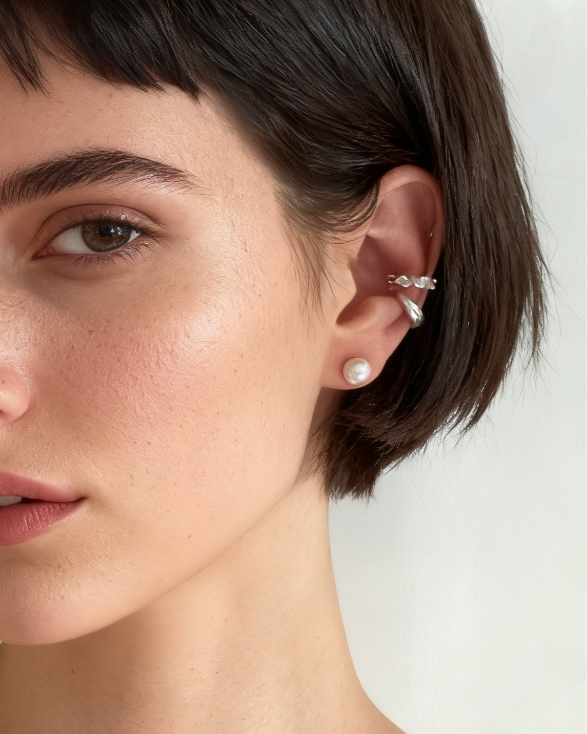 Close-up of a woman with short hair wearing earrings against a neutral background