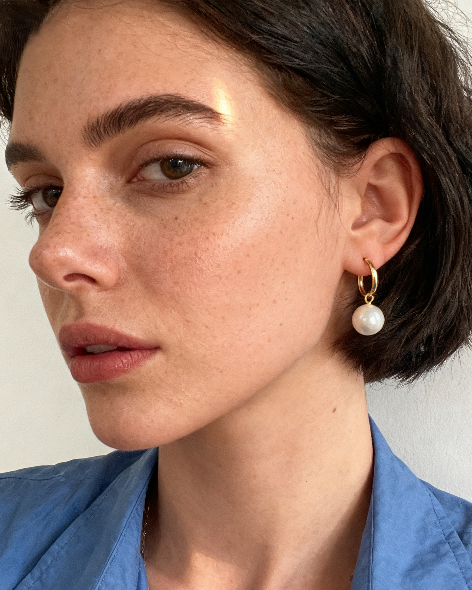 Close-up of a person wearing pearl earrings with a neutral background