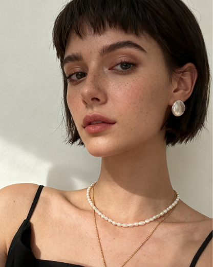 Woman wearing a pearl necklace and earrings against a neutral background