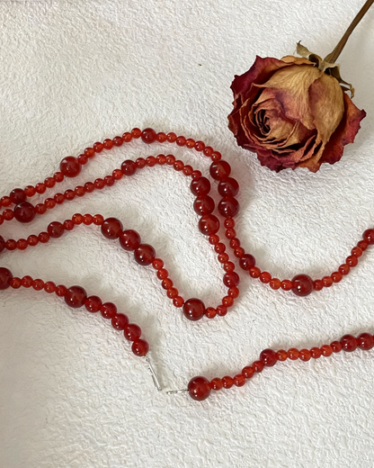 Red beaded necklace on a textured white surface with a dried rose.