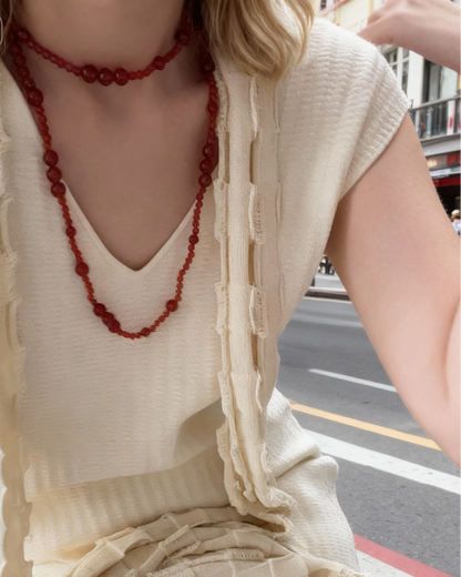 Person wearing a beige dress with a red beaded necklace on a street.