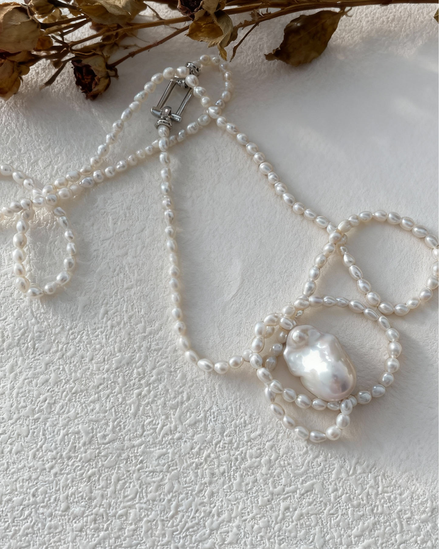 Pearl necklace with decorative elements on a textured white surface