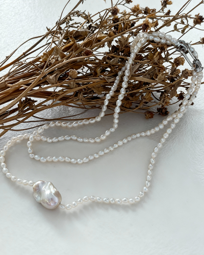 Pearl necklace with a large pearl pendant on a white surface with dried flowers.