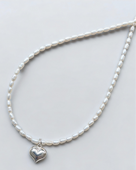 Pearl necklace with a silver heart pendant on a light gray background