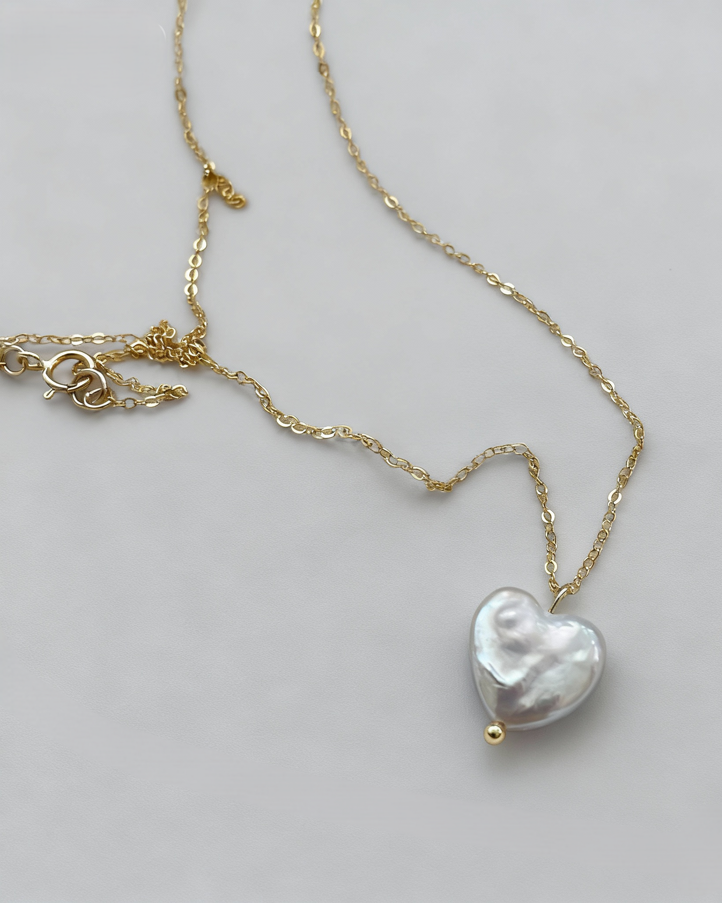 Gold necklace with a heart-shaped pearl pendant on a light gray background