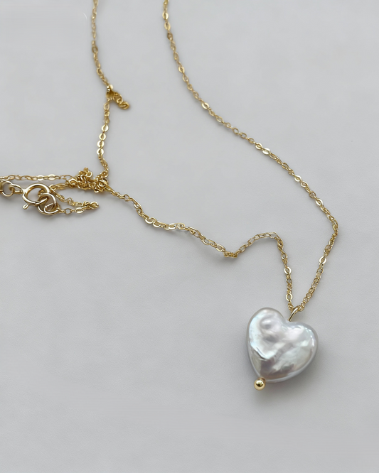 Gold necklace with a heart-shaped pearl pendant on a light gray background